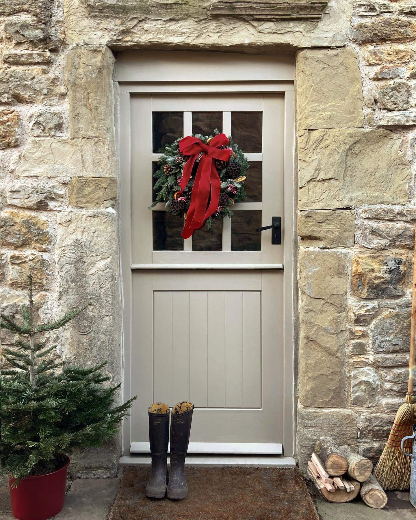 Outdoor front door entryway showcasing transition from Thanksgiving to Christmas decor featuring a classic wreath with large red velvet bow