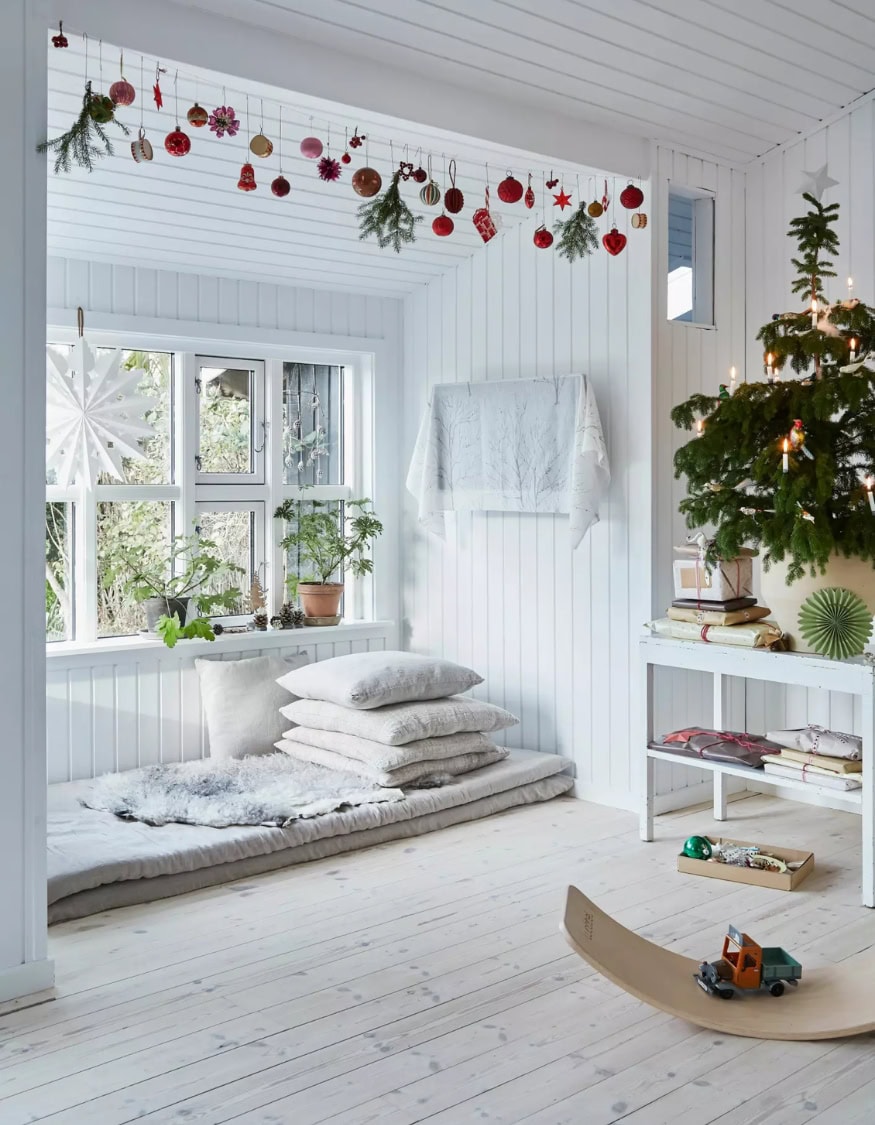 Kid-friendly Christmas decor ideas example featuring ornament garland hanging above a bay window nook