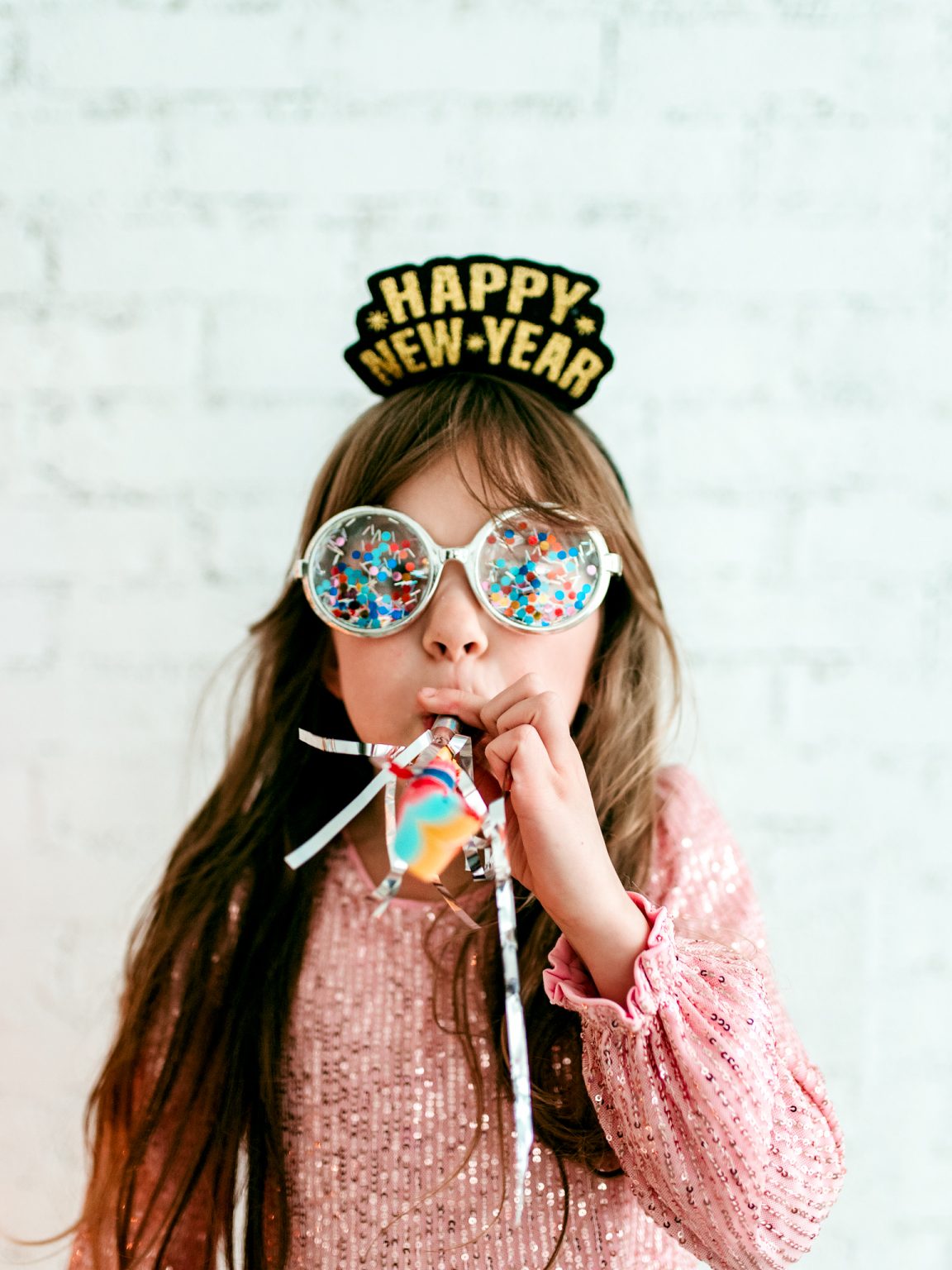 Celebrating New Year's eve with kids featuring a child having fun with a happy new year crown, and conffetti glasses
