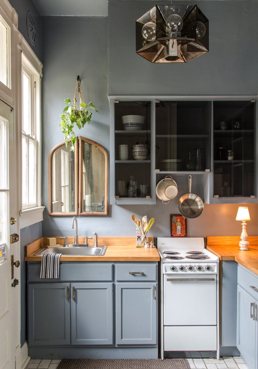 Example of how to use mirrors and lighting to enhance a space featuring a small kitchen with a small wooden mirror in cozy blue tones