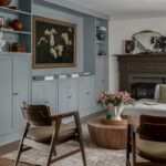 Living room with soft blue built-ins and a dark carved fireplace in a colonial home tour