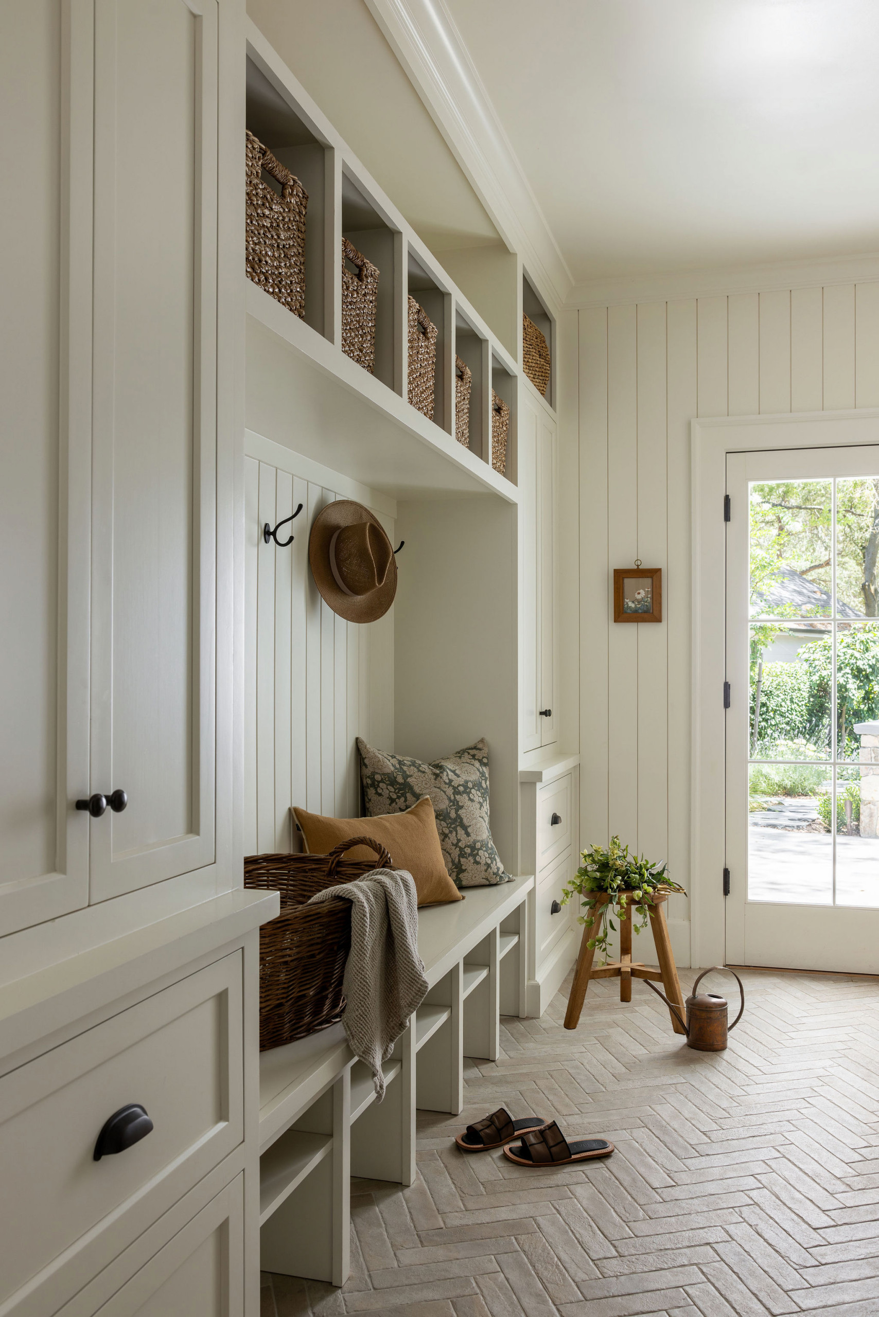 Mudroom with herringbone brick floor and woven storage baskets in a traditional home tour