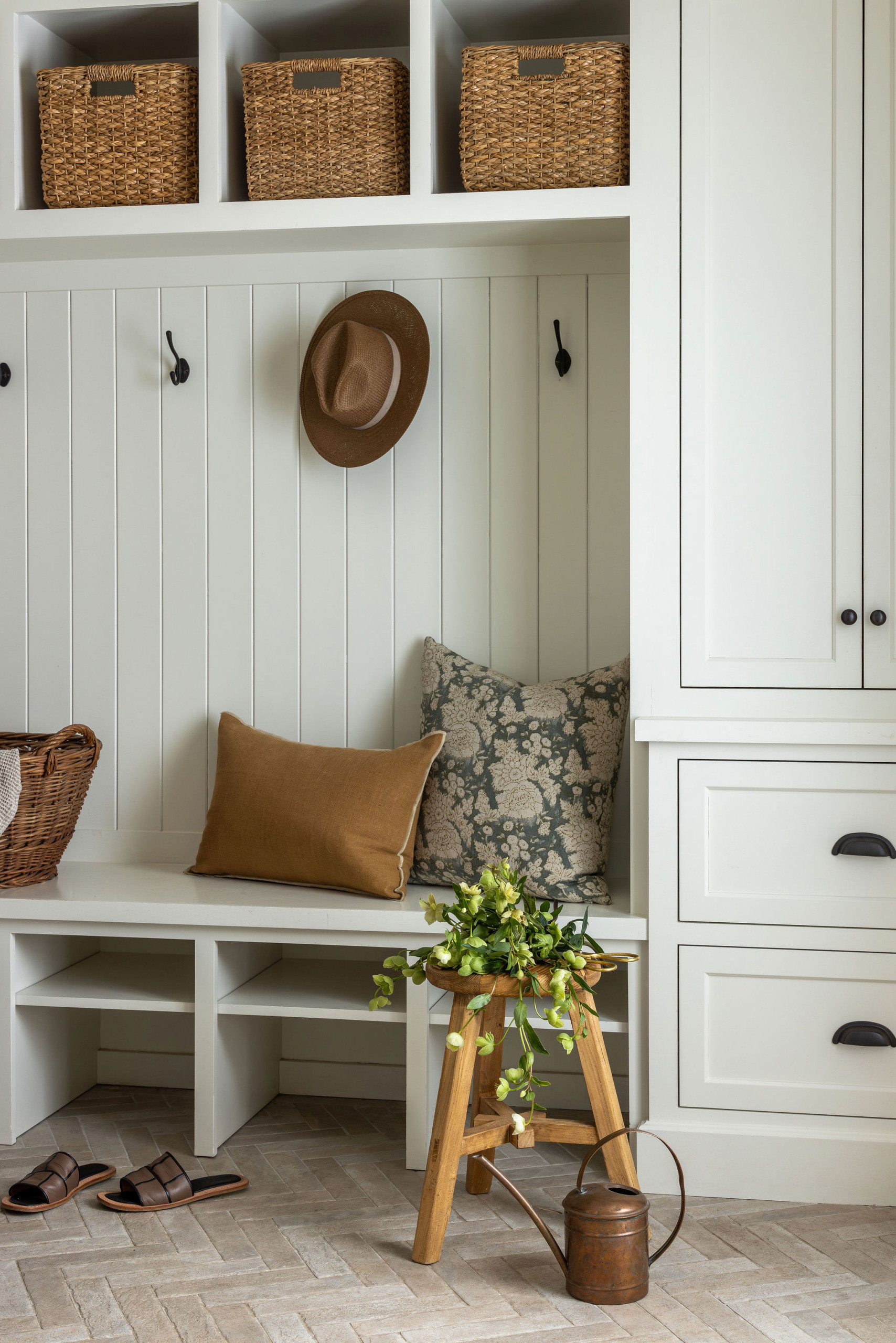 Mudroom with herringbone brick floor and woven storage baskets in a traditional home tour