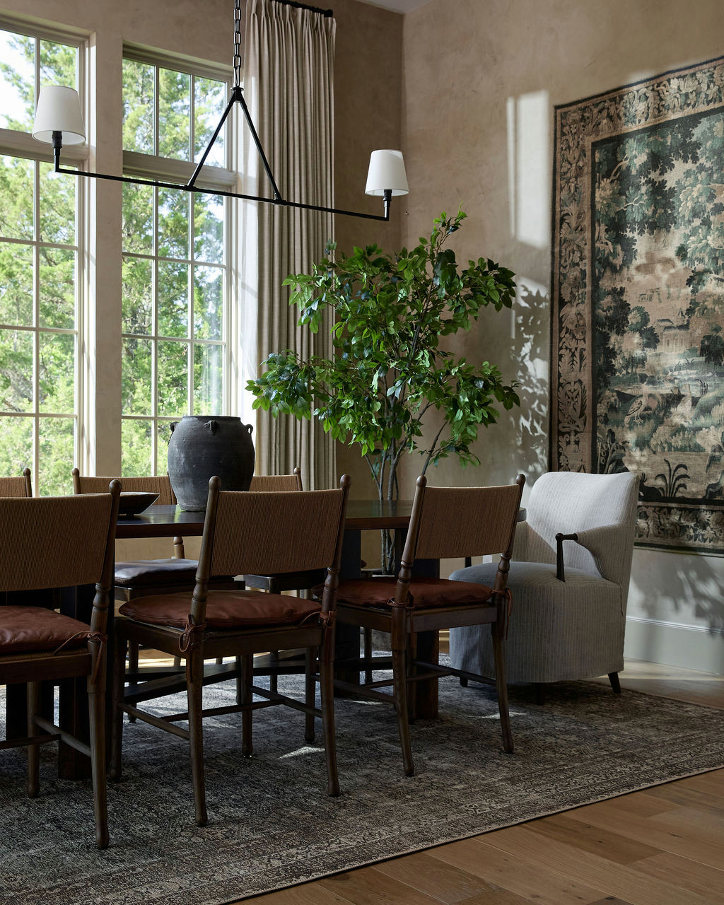 Mountain home tour dining room with plaster walls, a large tapestry, and woven-back chairs with leather cushions.