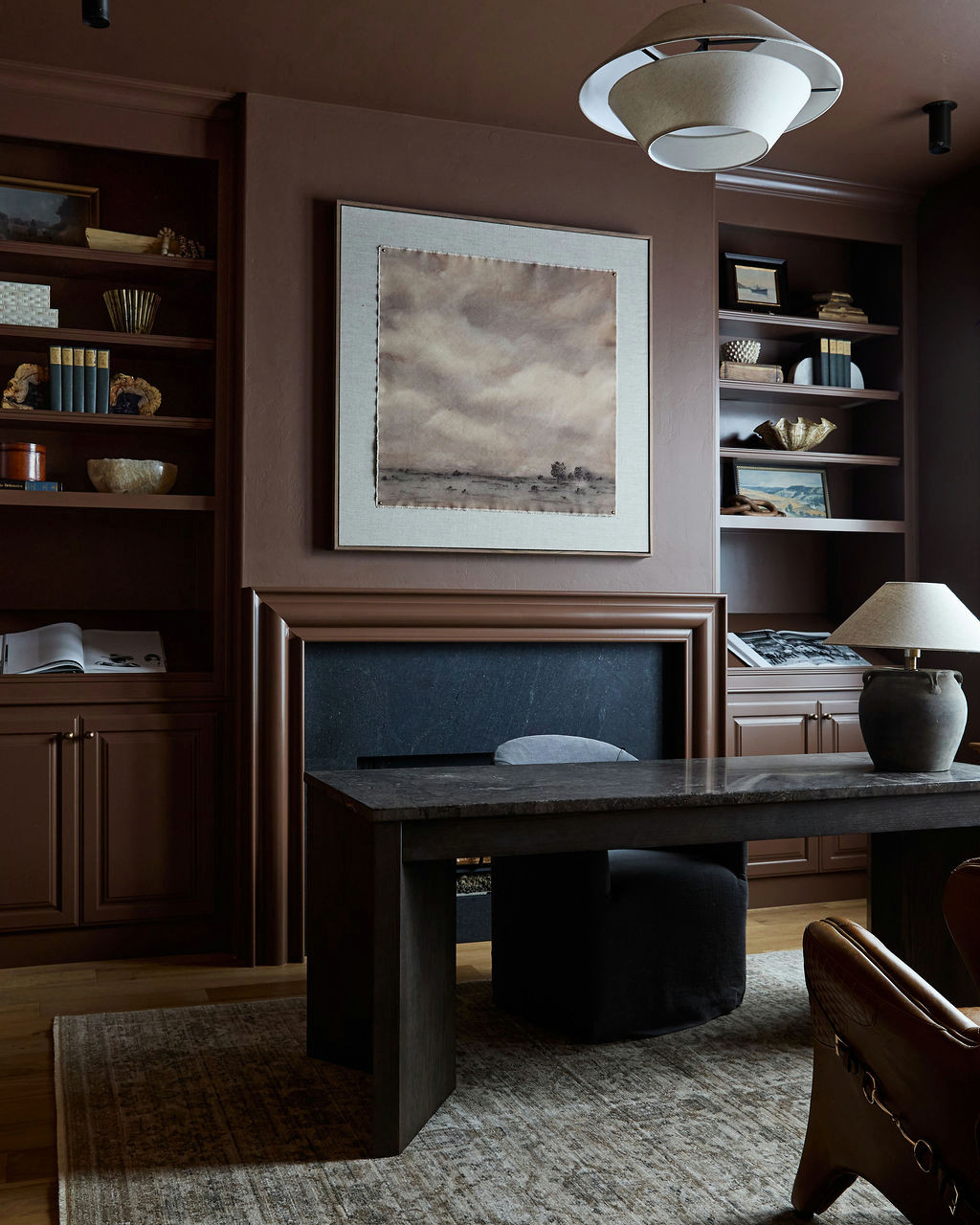 Mountain home tour office in chocolate brown with matching built-ins, a dark stone fireplace, and a stone-topped desk.