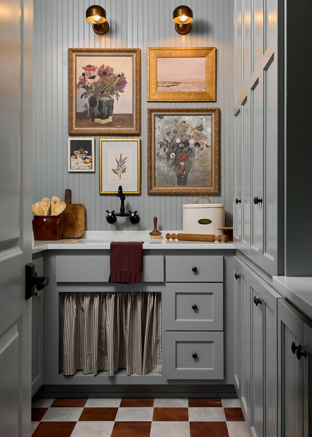 Mountain home tour laundry room with blue-gray beadboard, a gilded-frame gallery wall, and checkerboard floor.