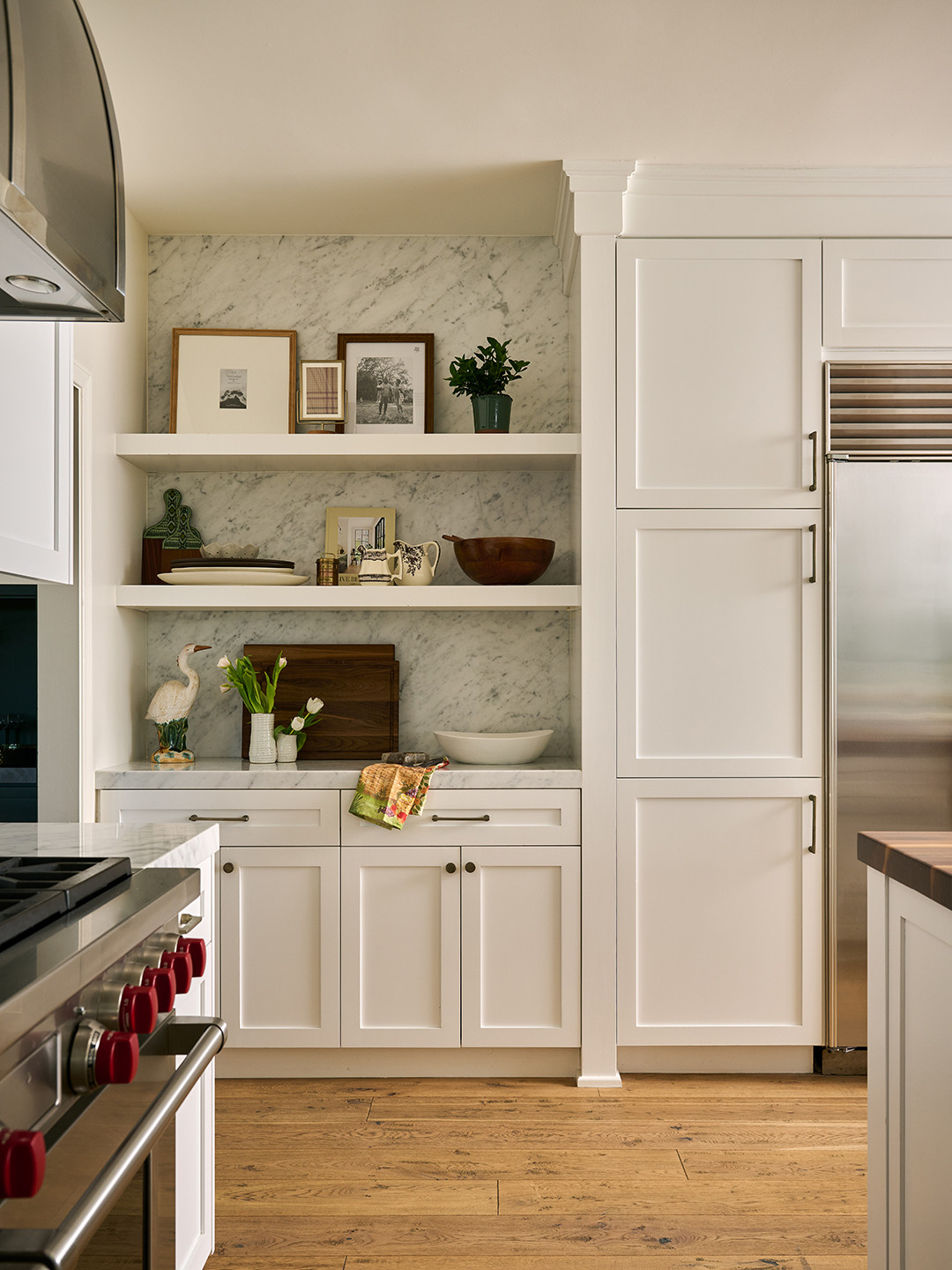 Kitchen with white shaker cabinetry and open shelves against Carrara marble in a Mediterranean home tour